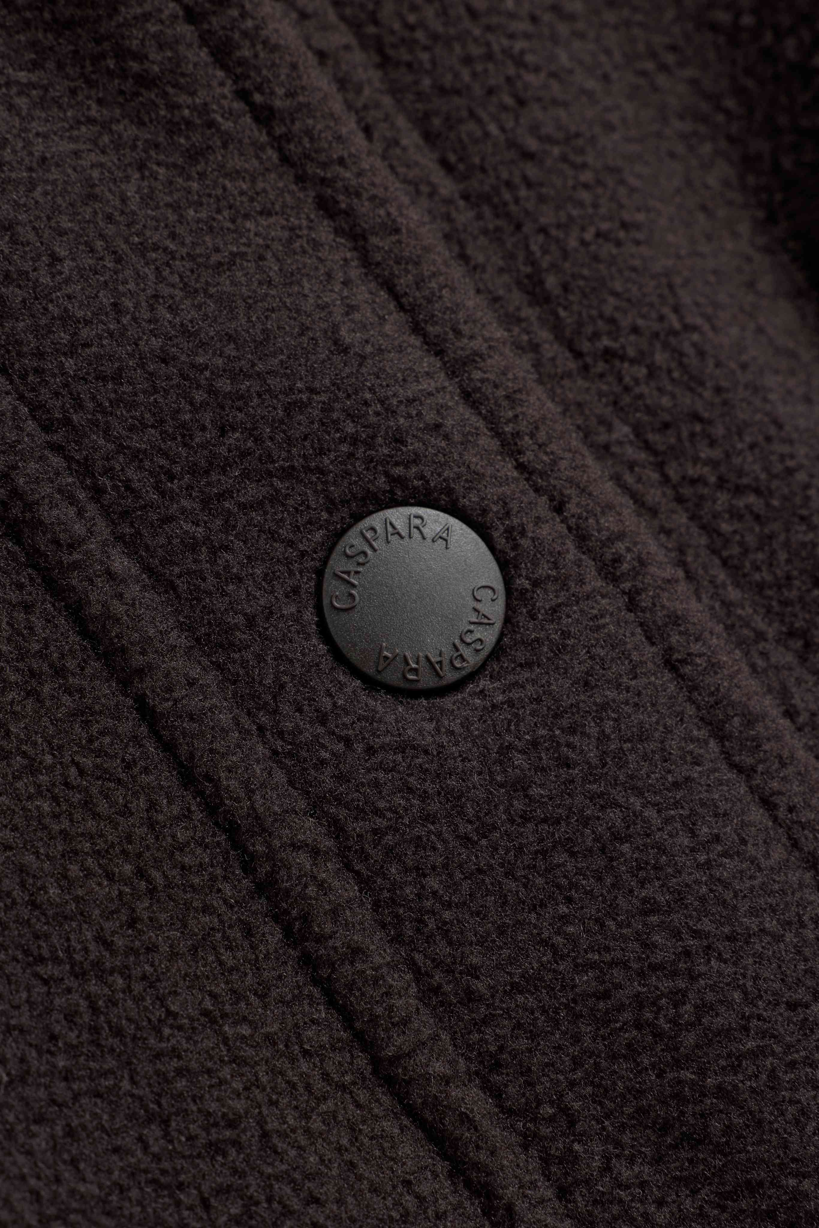 Close-up of an engraved snap button on an espresso CASPARA polar fleece pullover.